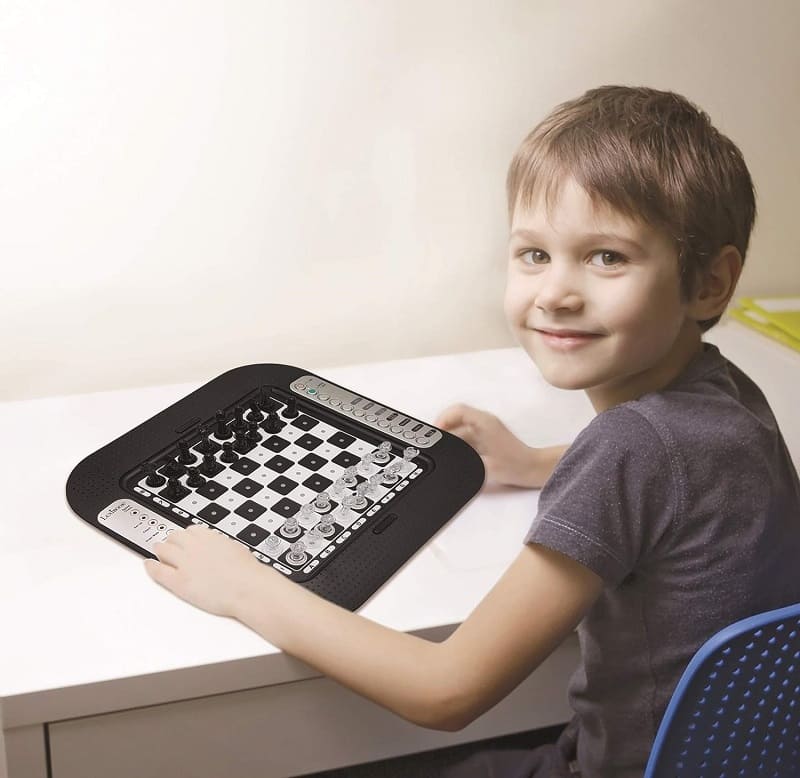 Bambino sorridente gioca a scacchi su un tavolo luminoso.